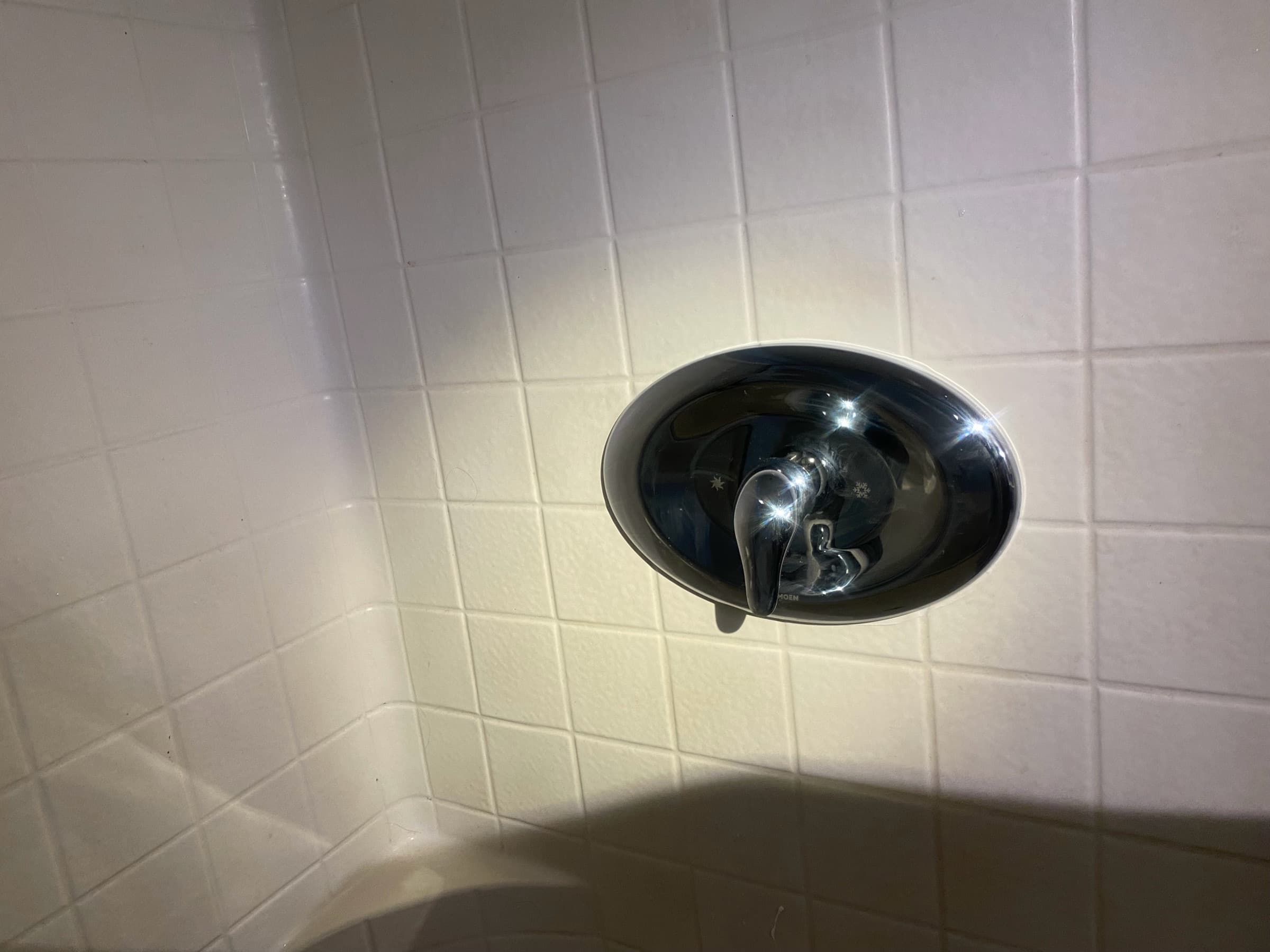 Moen single-handle shower valve trim in polished chrome on a white tile shower wall, replacing an old three-handle assembly